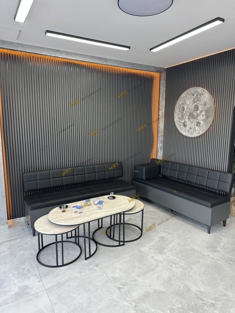 Bornova berber salonu bekleme bölümünde ikili sandıklı koltuklar ve oval orta sehpalar